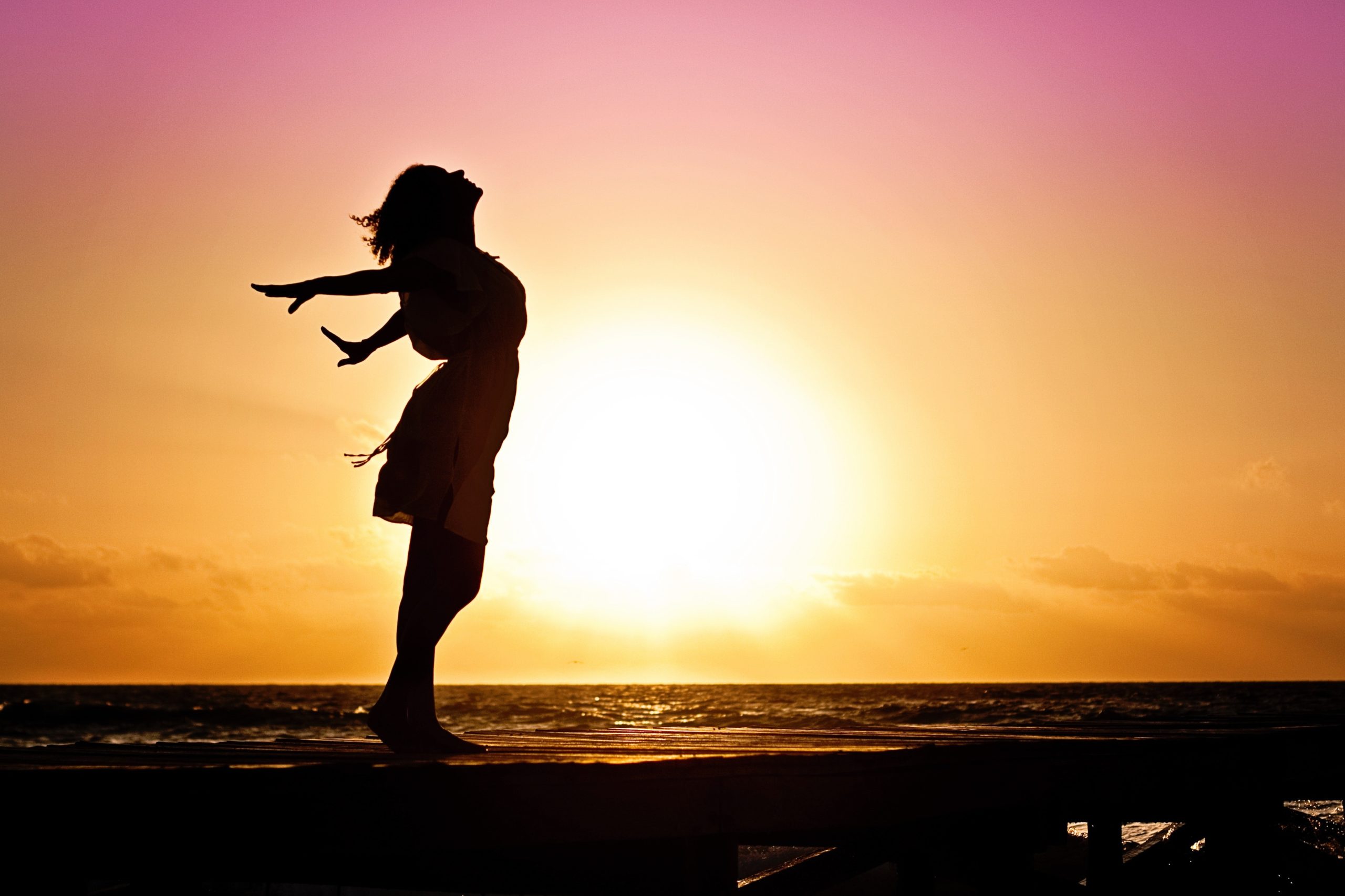 a woman extends her arms free and happy during sunset